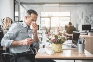 A man blowing his nose in an office.