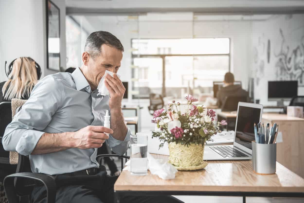 A man blowing his nose in an office.