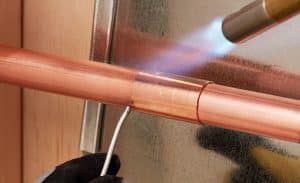 A person is working on a copper pipe with a torch.