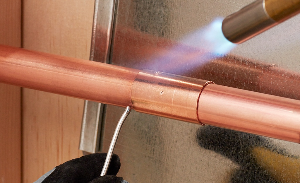 A person is working on a copper pipe with a torch.